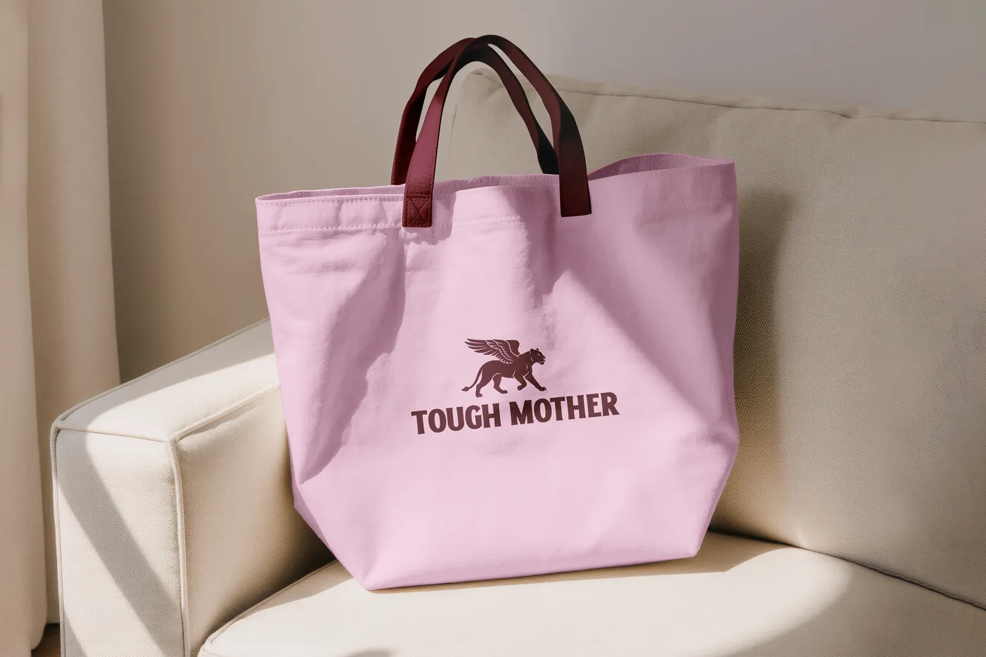 A pink Tough Mother tote bag with the winged lioness, on a chair
