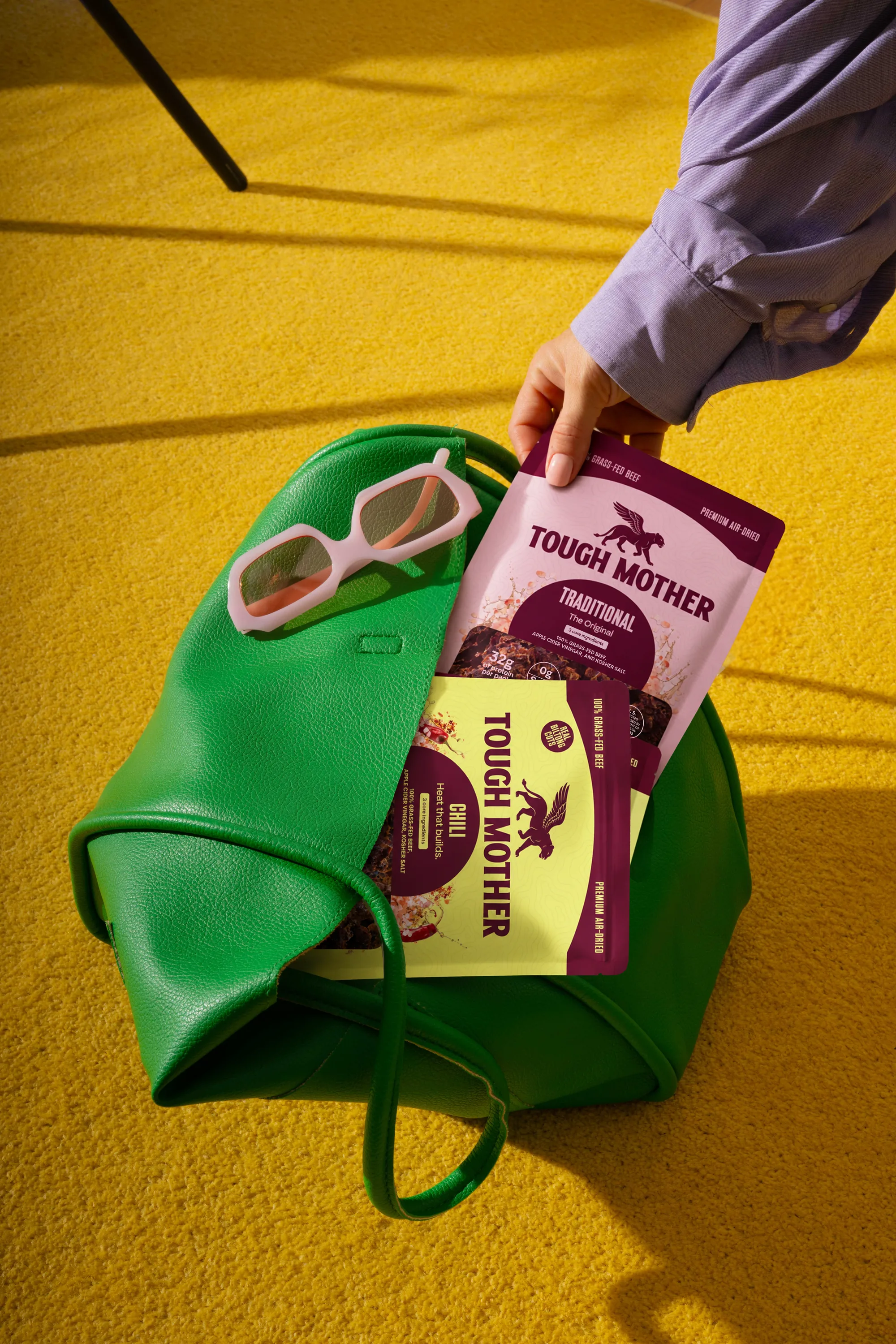 Traditional and Chili pouches going into a green leather tote on a yellow carpet